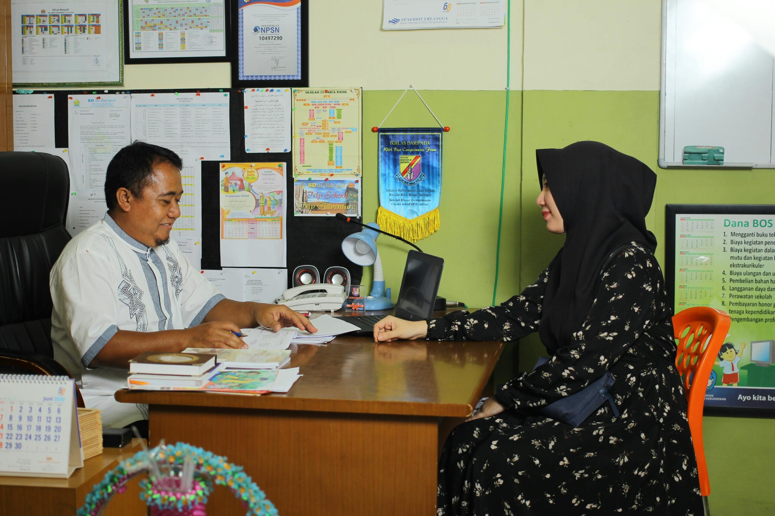 A teacher and parent meeting over school matters in an Indonesian office setting.