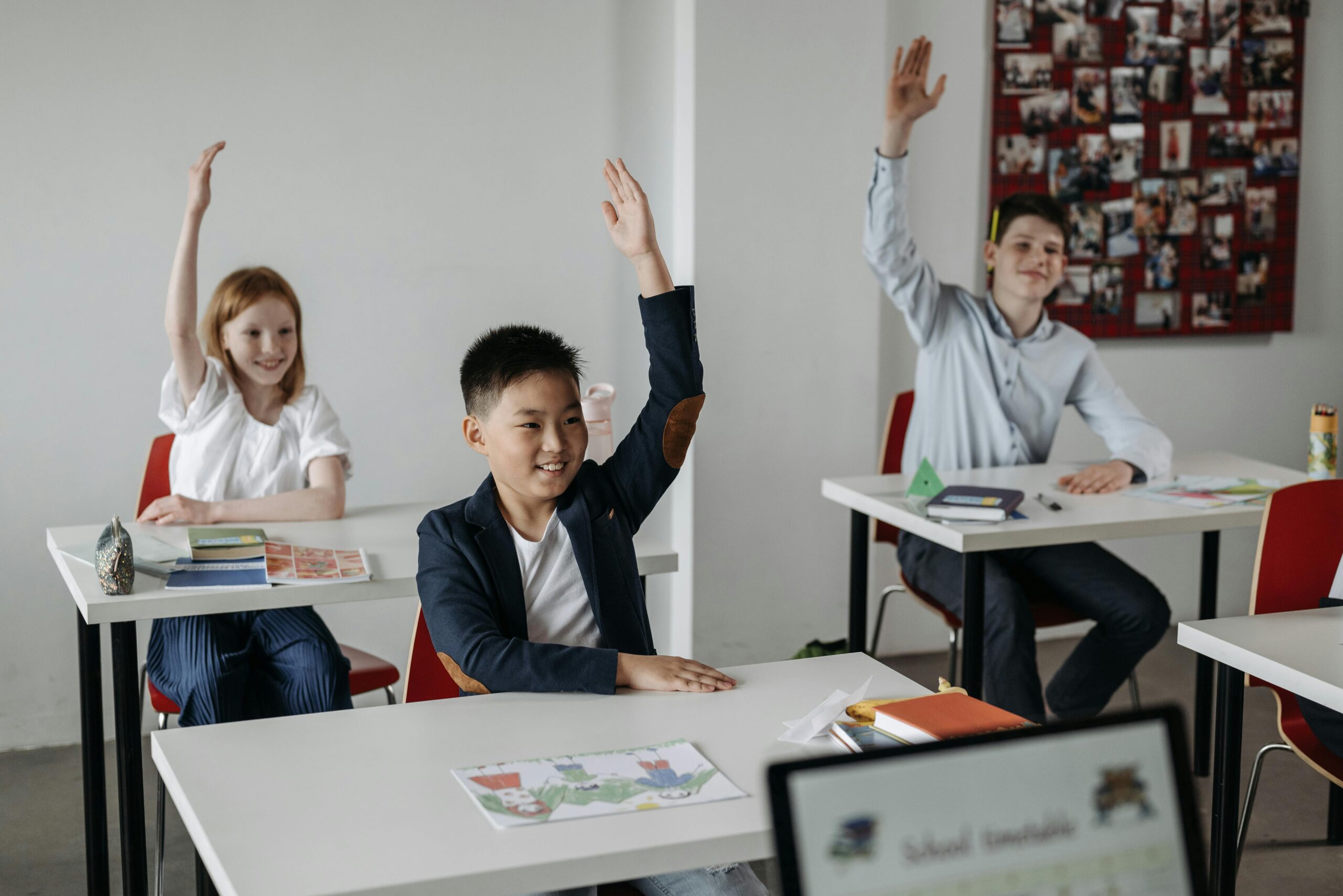 Diverse group of students actively participating in a classroom setting, raising hands for recitation.